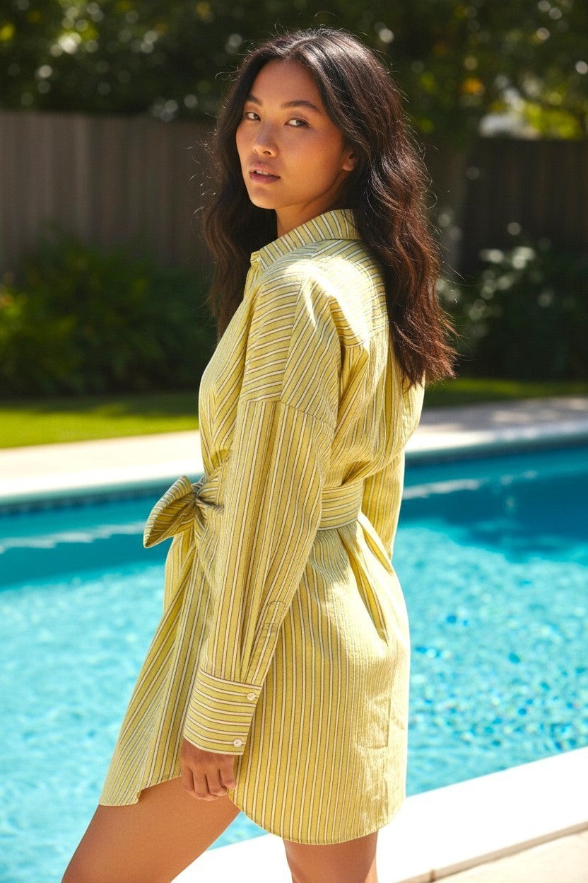 State of Georgia yellow and white striped linen shirt dress with tie waist and button cuffs, worn by a woman by a pool.